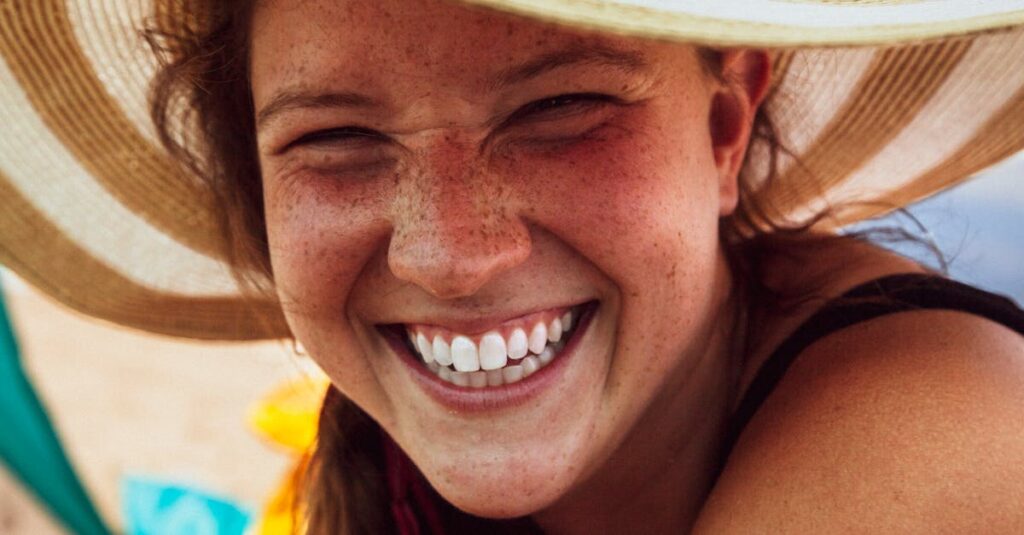 Close-up of a smiling woman with freckles wearing a sun hat, exuding happiness.