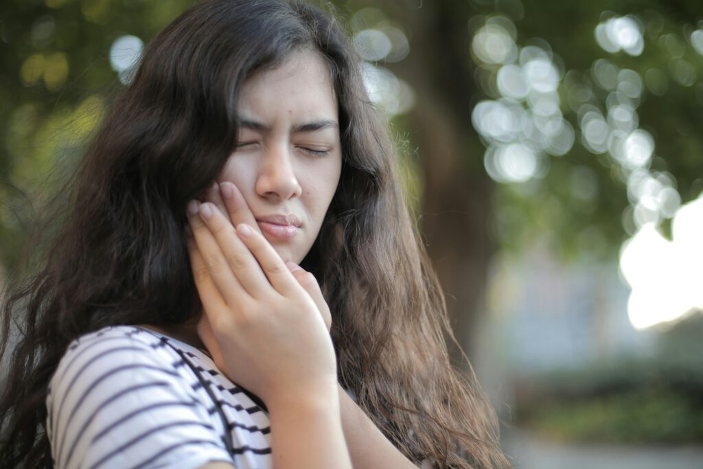 Portrait of a young woman feeling toothache, showing discomfort outdoors with a pained facial expression.